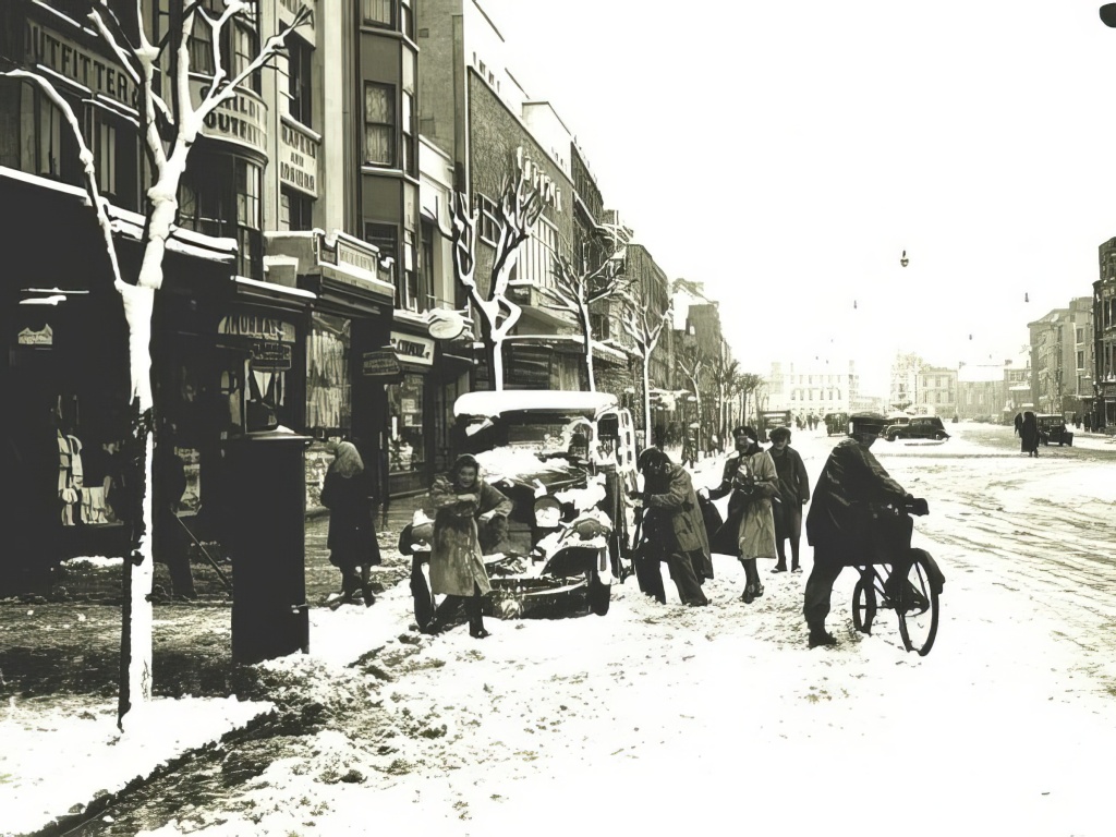 People on a snowy street, probably in the middle of fighting with snowballs in front of a parked car while a cyclist looks at the camera
